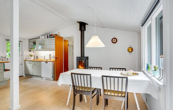 A dining area with a white table and chairs, a wood-burning stove, and a window with candles.