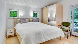 Et soveværelse med en stor seng, to sengeborde, en stol, et spejl og en skydedør til en balkon.