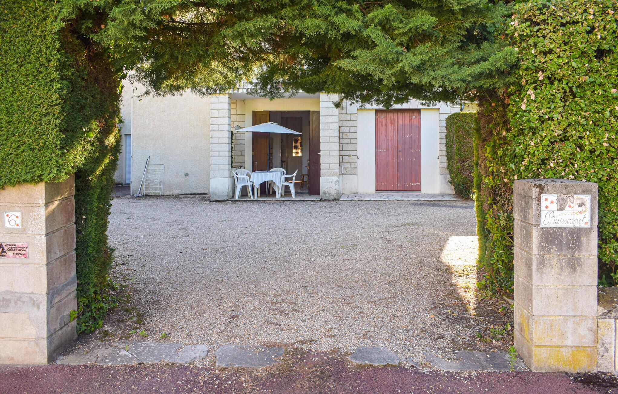 A gravel courtyard with a table and chairs under a canopy, a building entrance, and a red door.