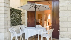 Una mesa redonda con mantel blanco y seis sillas de plástico blancas, en un patio empedrado.