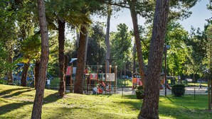 Un parque con juegos infantiles, árboles y una zona delimitada por una cerca.