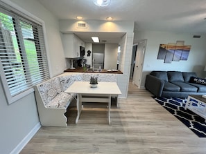 Un espacio habitable compacto con kitchenette, una zona de comedor con un banco de temática de café, un sofá y una alfombra estampada.