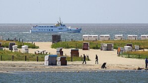 Ein Strand mit Strandkörben, ein Schiff im Hintergrund und ein sandiger Uferstreifen.