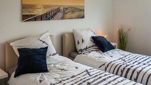 Ein Hotelzimmer mit zwei Betten, jeweils ausgestattet mit passenden Kissen und gestreifter Bettwäsche. An der Wand hängt ein Gemälde, das einen Sonnenuntergang über einem Steg zeigt.