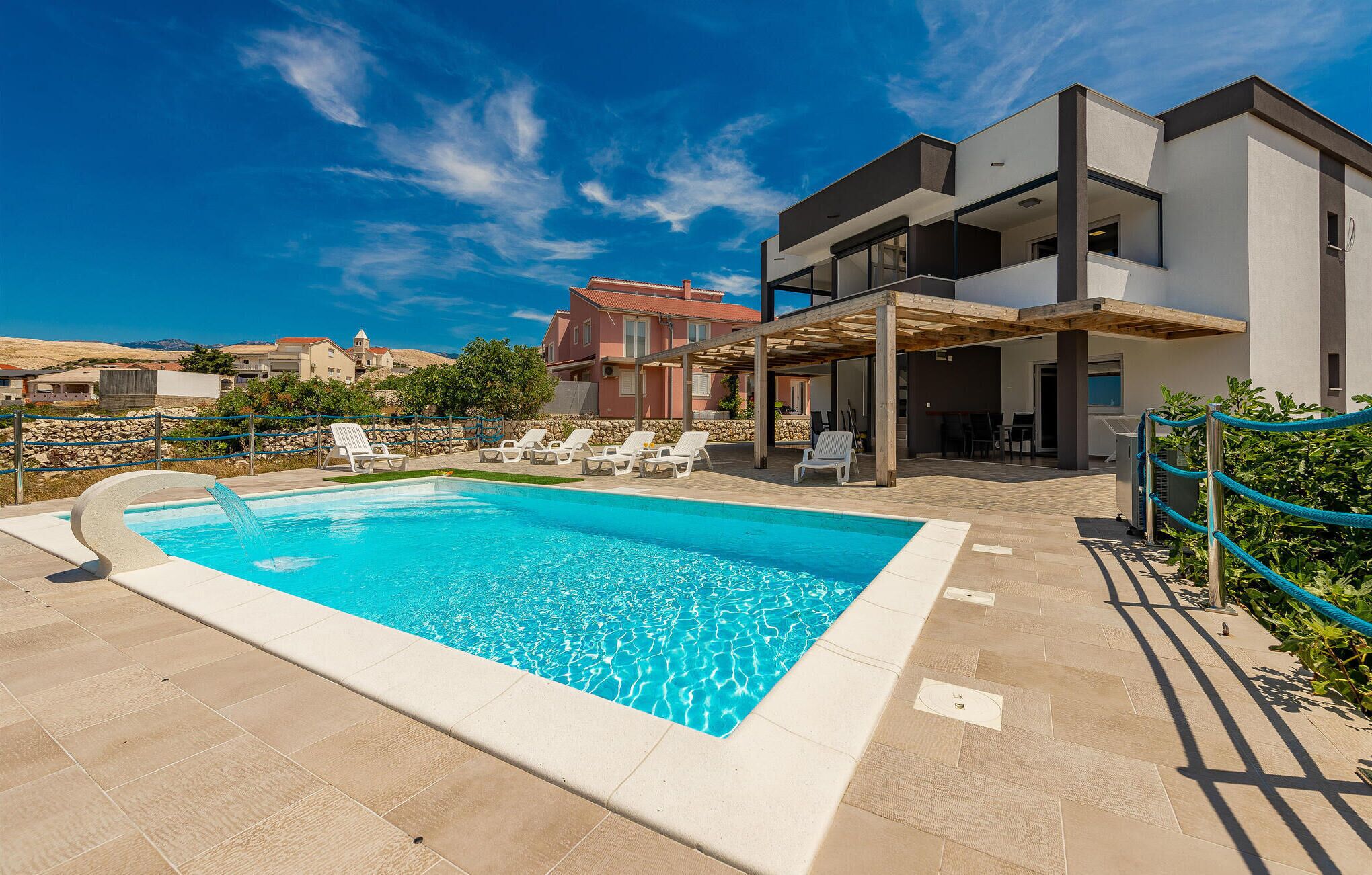 Un área de piscina moderna con una piscina rectangular, sillas de descanso y una zona de estar cubierta.