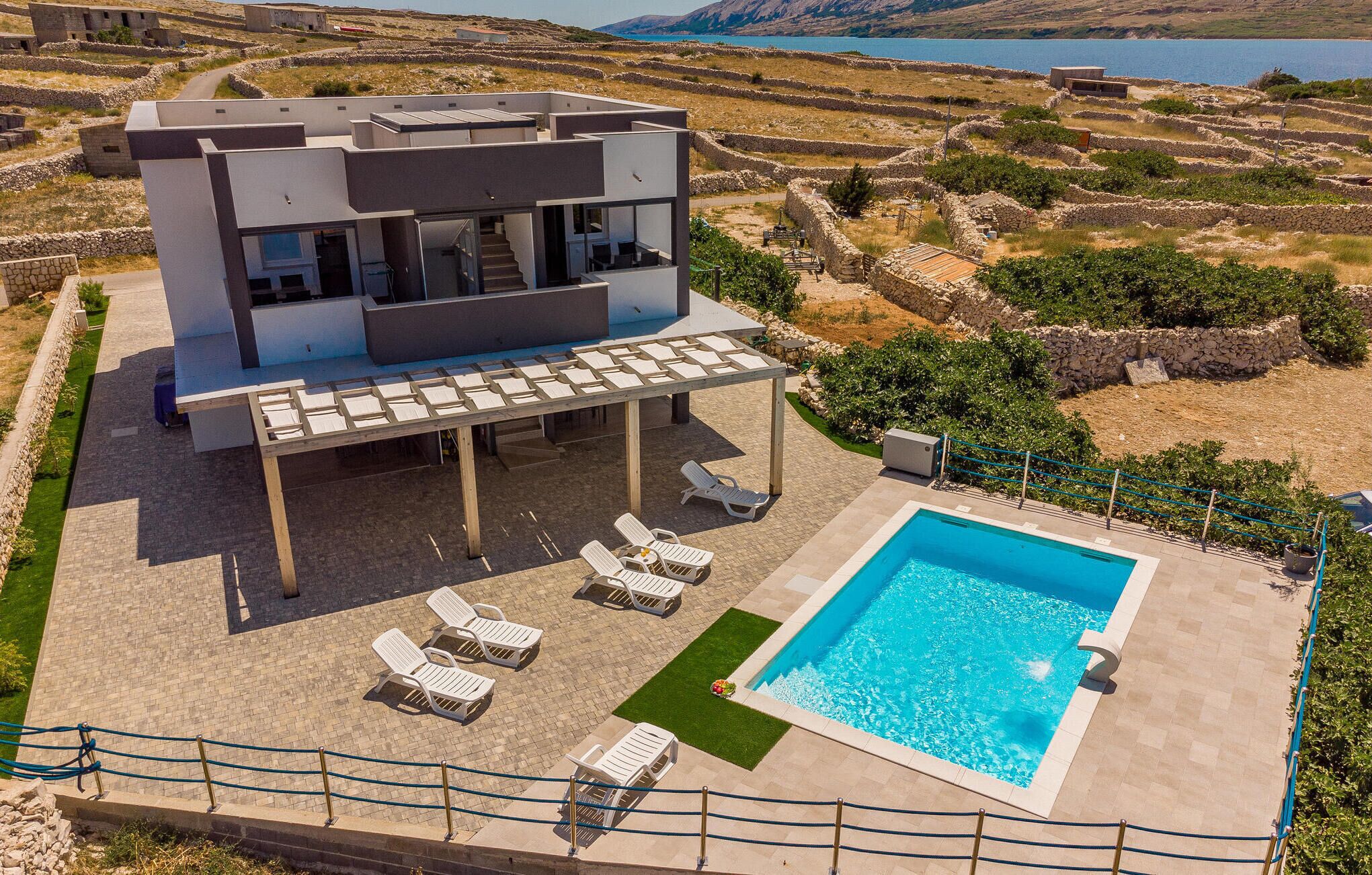 A modern villa with a pool, outdoor seating, and a view of terraced fields and water.