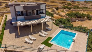 En moderne villa med pool, udendørs møbler og udsigt til terrasserede marker og vand.