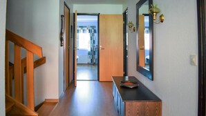 Un pasillo con suelo de madera, una escalera de madera y una puerta de madera que da a otra habitación.