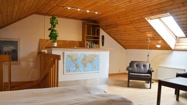 Un dormitorio acogedor en el ático con techo inclinado, un mapa mundial en la pared, una estantería, un sillón de cuero y un escritorio.