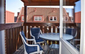 A covered outdoor seating area with a round table and two chairs, a wooden deck, and a view of a house with a red roof.