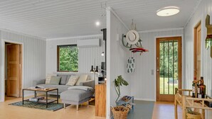 Ett modernt vardagsrum med en soffa, ett soffbord och ett stort fönster. Det finns en dörr som leder ut till ett utomhusområde.
