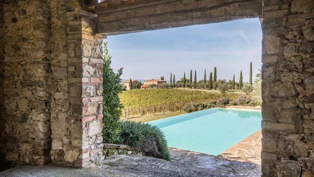 A stone-walled pool area with a clear view of a vineyard and distant buildings. - Awesome home in Castellina in Chianti (Castellina in Chianti)