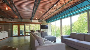 A spacious living area with a large sofa, a smaller sofa, and a coffee table. There is a television mounted on the wall and a large window providing a view of the outdoors. - Secluded 20 acre 10BR ultra contemporary retreat (Manchester-by-the-Sea)