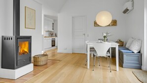 Eine moderne Küche mit Kaminofen, einem Essbereich mit weißem Tisch und Stühlen und einer gemütlichen Sitzecke mit blauem Sofa.