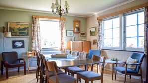 Uma sala de jantar com mesa de madeira, cadeiras, um lustre e janelas amplas.
