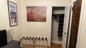 A bedroom with a bed, a wall-mounted lamp, a drying rack, a closet with hanging clothes, and a door to another room. - Stylish, Inviting 2-BR near Logan Square and Wrigley Field (Chicago)