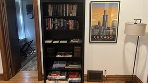 A room with a bookshelf filled with books, a framed picture of the Chicago skyline, and a floor lamp. - Stylish, Inviting 2-BR near Logan Square and Wrigley Field (Chicago)