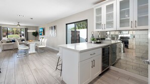 Une cuisine moderne avec des meubles blancs, un îlot central et un coin repas comprenant une table et des chaises blanches.