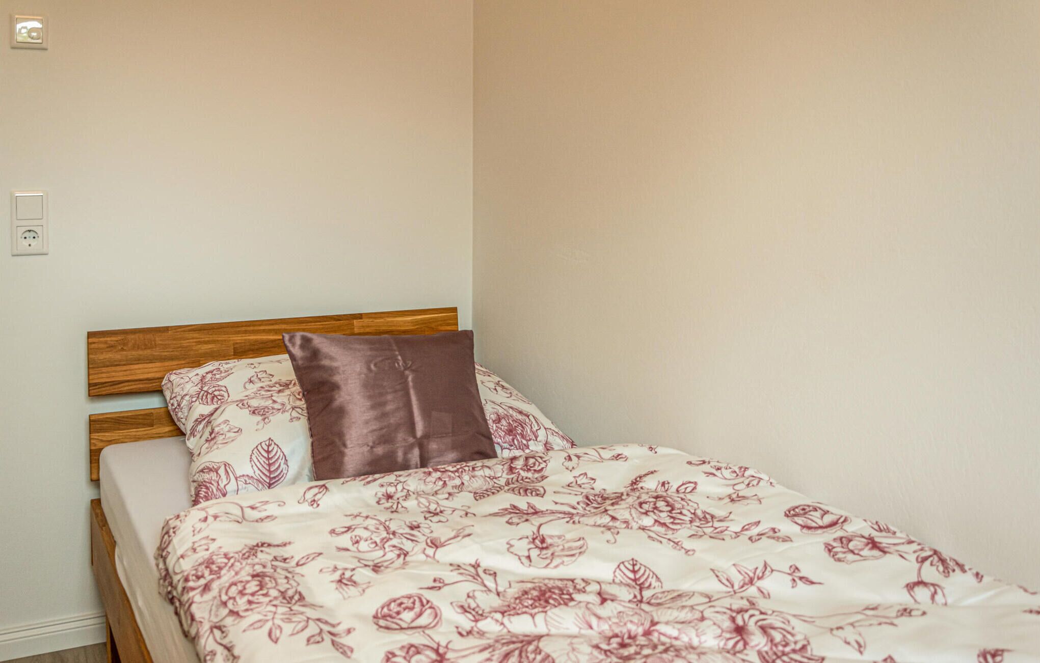 A single bed with a wooden headboard, a floral-patterned bedspread, and a brown pillow.