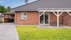A brick house with a tiled roof, a satellite dish, a covered patio with chairs, and a small lawn. - 2 bedroom beautiful home in Stapel (Stapel)