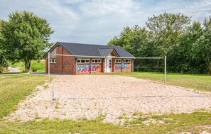 Play volleyball in a scenic outdoor court surrounded by lush greenery and a unique brick building.