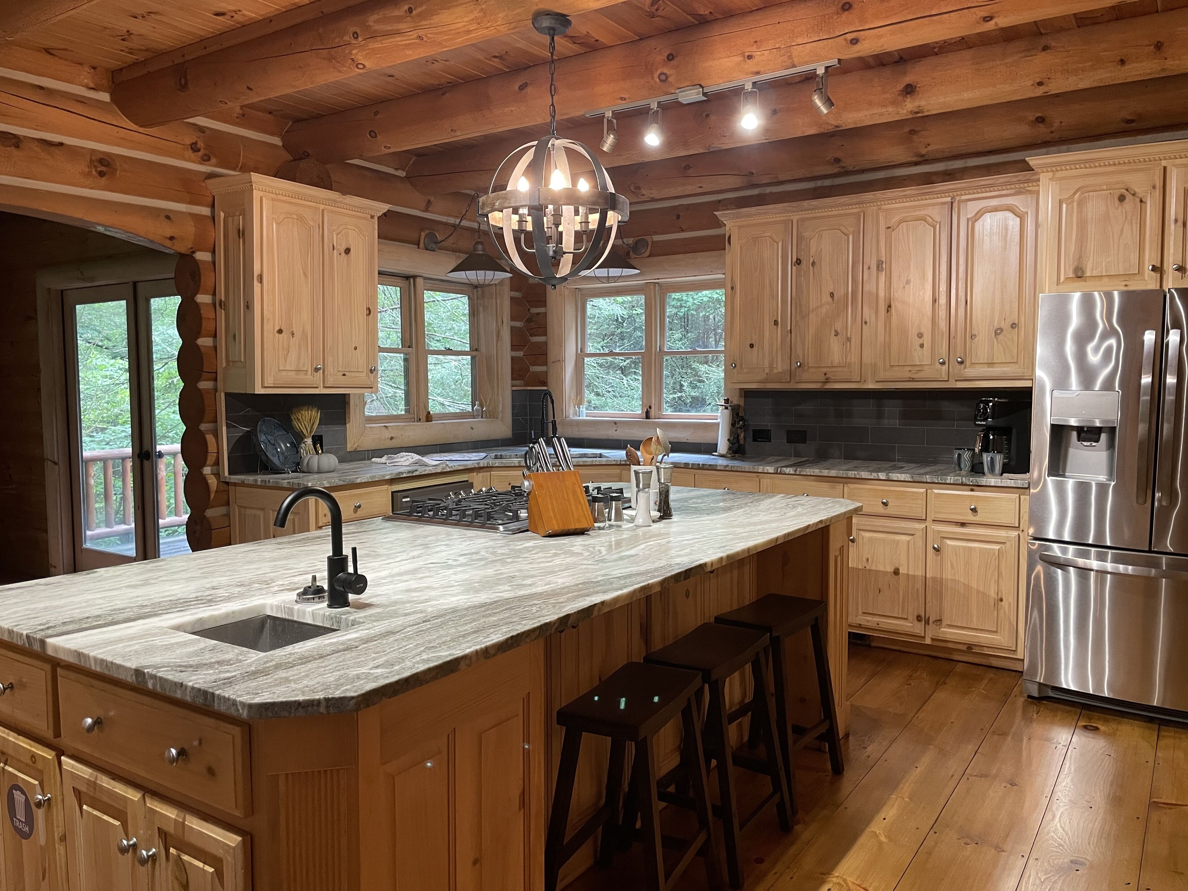Une cuisine spacieuse avec des meubles en bois, un grand îlot central doté de tabourets, un réfrigérateur en acier inoxydable et un lustre.