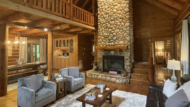 A spacious log cabin interior with a stone fireplace, multiple seating areas, and a balcony overlooking the interior. - Spacious cabin w/Hot Tub , 10 minutes from downtown Blue Ridge. (Cherry Log)