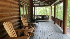 A wooden cabin with a porch, a bed, and two Adirondack chairs. - Spacious cabin w/Hot Tub , 10 minutes from downtown Blue Ridge. (Cherry Log)