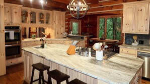 A spacious kitchen with wooden cabinets, a marble island, and a hanging light fixture. - Spacious cabin w/Hot Tub , 10 minutes from downtown Blue Ridge. (Cherry Log)