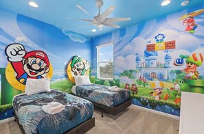 A room with two beds, a ceiling fan, and a mural with Mario and Luigi characters.
