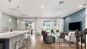 Une cuisine moderne dotée d’un îlot central, de tabourets de bar, d’un coin repas avec un canapé et d’un téléviseur fixé au mur.
