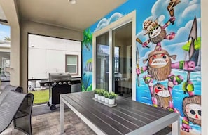 An outdoor patio with a grill, a table with potted plants, and a mural with cartoonish characters.