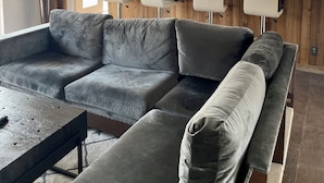 Un salon moderne avec un canapé d’angle, une table basse et un coin cuisine doté de meubles blancs et d’une fenêtre.