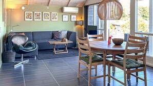 Ein modernes Wohnzimmer mit einer Couch, einem Esstisch mit Stühlen, einer Hängeleuchte und Bildern an den Wänden.
