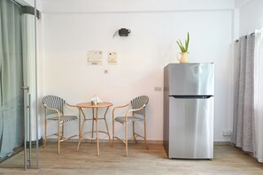 A small kitchenette with a refrigerator, two chairs, a table, and a potted plant.