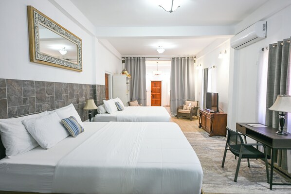A hotel room with two beds, a desk, a chair, a TV, a mirror, and a door leading to another room.