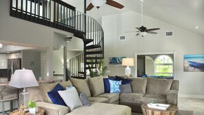 A spacious living room with a large sectional sofa, two wooden coffee tables, a ceiling fan, and a spiral staircase. - Luxury Island Escape @ Palm Tree Villa: Private Rooftop Deck & Saltwater Pool (Bookelia)