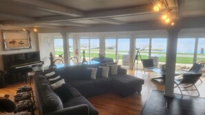 Amplia sala de estar con un sofá modular grande, un piano y vista a la playa a través de amplios ventanales.