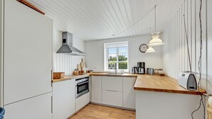 A modern kitchen with white cabinetry, a wooden countertop, a built-in oven, and a window providing natural light. - Cozy home in Ulfborg with kitchen (Ulfborg)