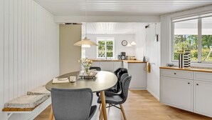 A modern kitchen with white cabinetry, a wooden dining table with two chairs, and a window with a view of greenery. - Cozy home in Ulfborg with kitchen (Ulfborg)