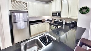 Una cocina con armarios blancos, electrodomésticos de acero inoxidable, un lavamanos doble y una encimera negra.