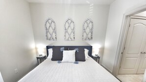 Una cama bien hecha con una colcha blanca acolchada, un cabecero oscuro y tres elementos decorativos colocados en la pared.
