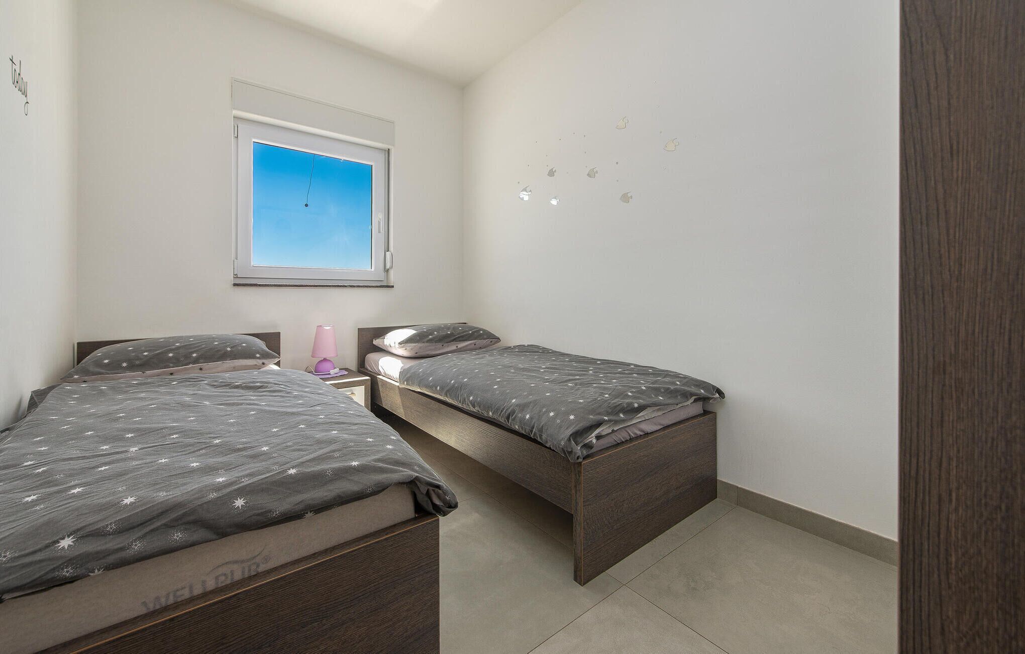 A small, well-lit bedroom with two single beds, a window with a view of the sky, and a wall with a few decorative elements.