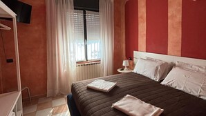 Ein Hotelzimmer mit einem Bett, einem Nachttisch, einer Lampe und einem Fenster mit Vorhängen.