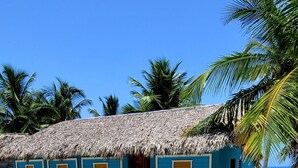 Una cabaña con techo de paja, cerca blanca, paredes azules y puerta de madera.