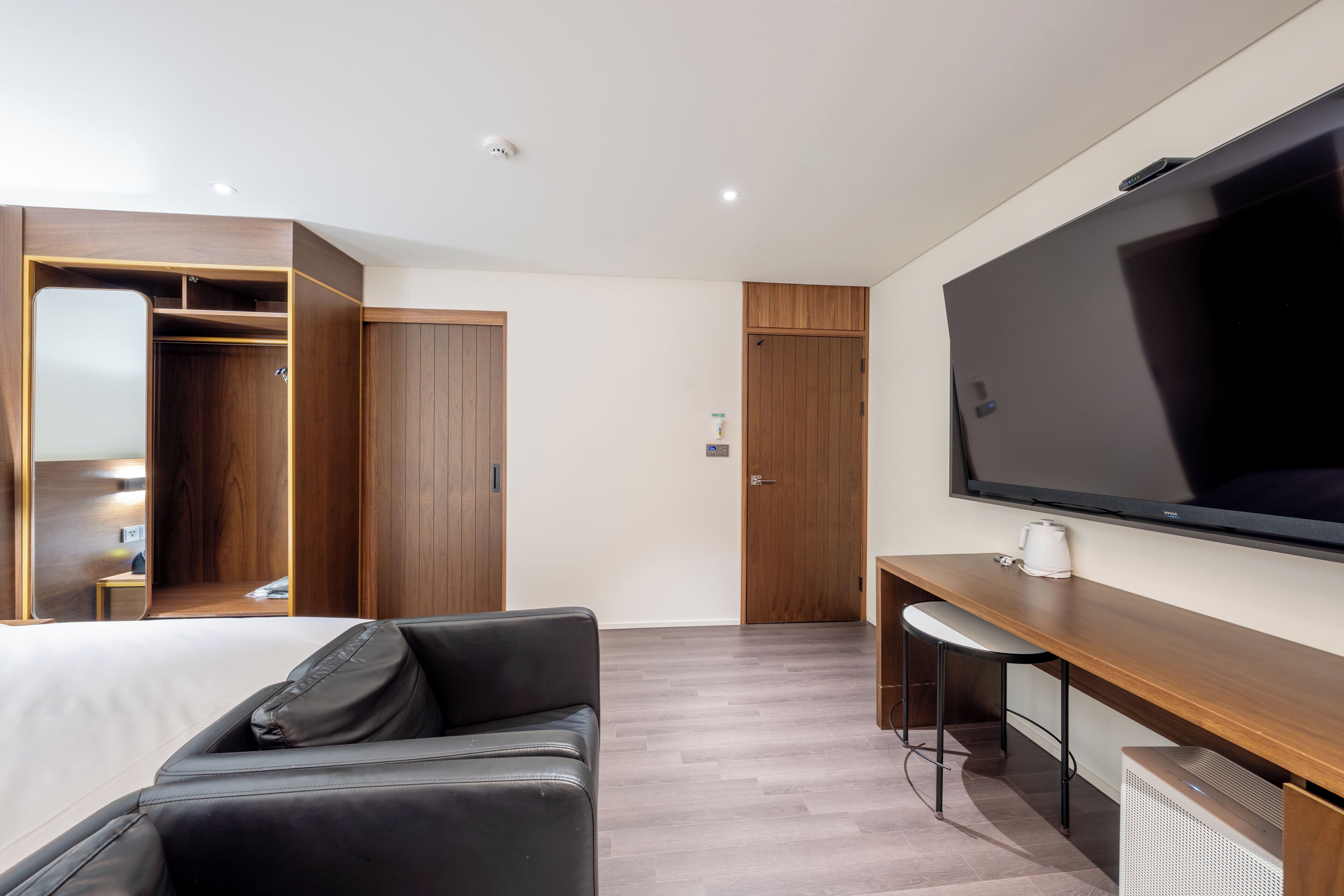 A modern hotel room with a large bed, a desk with a chair, a television, a wardrobe, and a mirror.