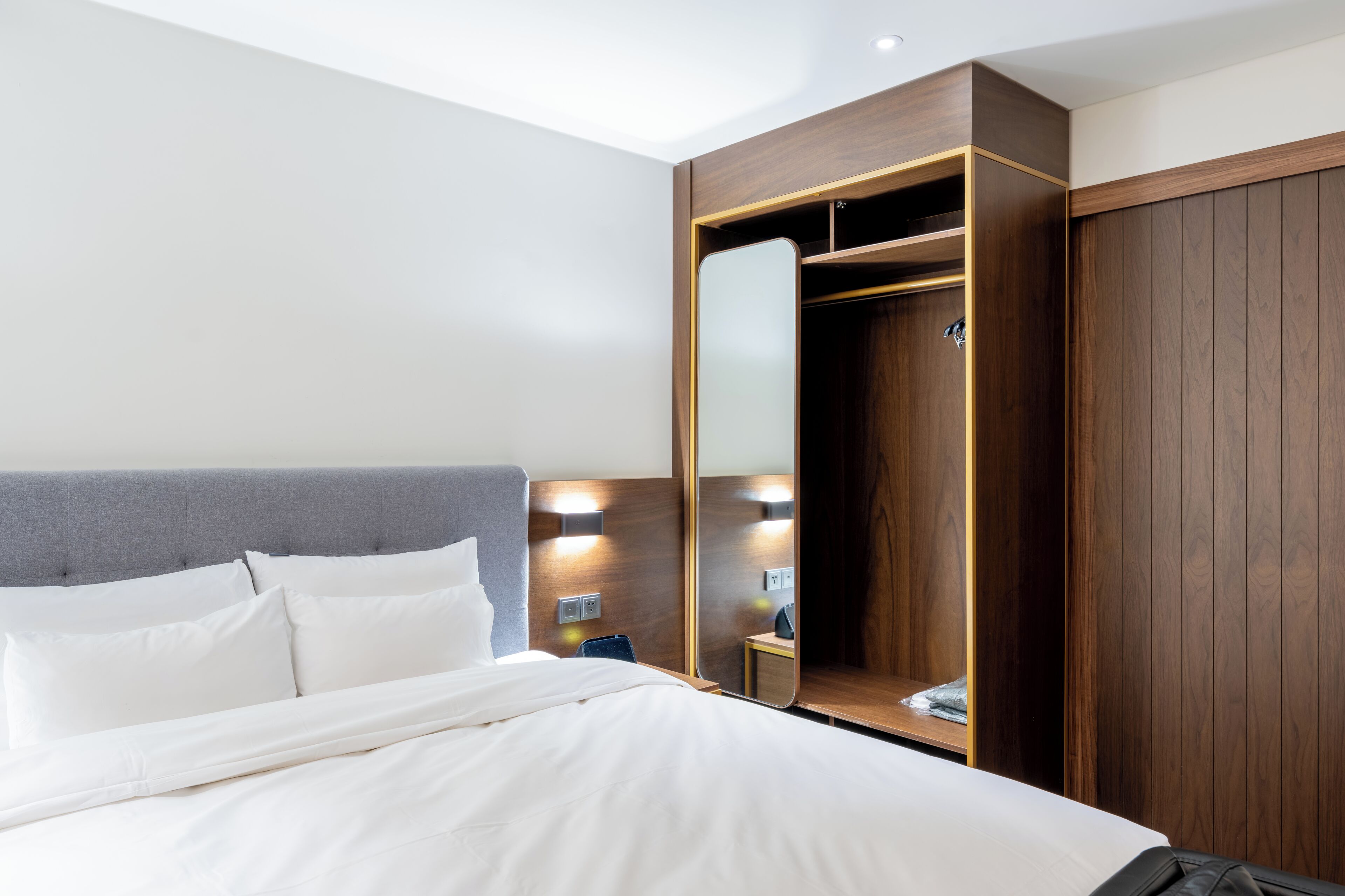 A hotel room with a bed, a wardrobe, a mirror, and a bedside table.