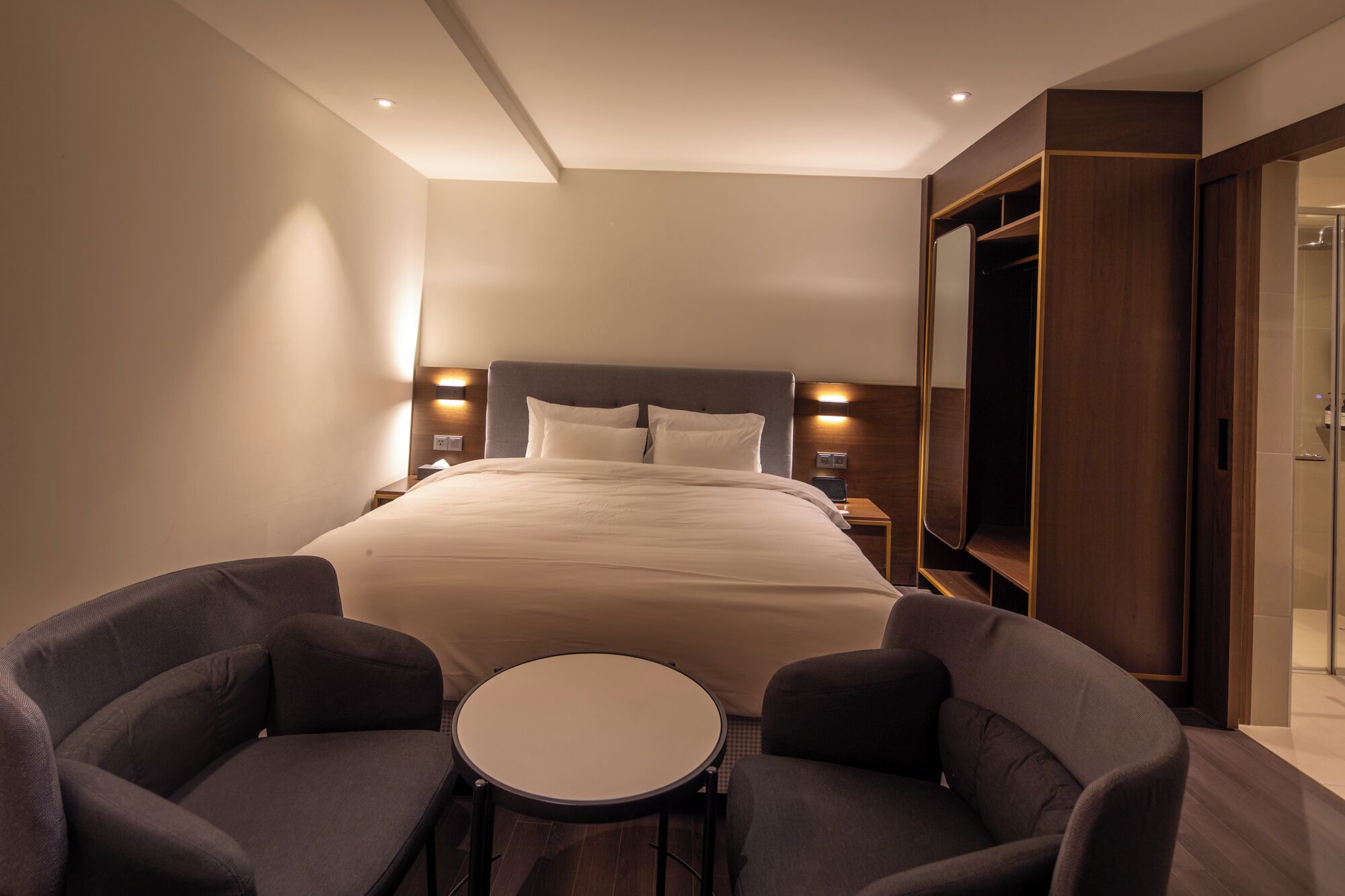 Una habitación de hotel con una cama grande, mesitas de noche, un televisor, un armario y dos sillones.