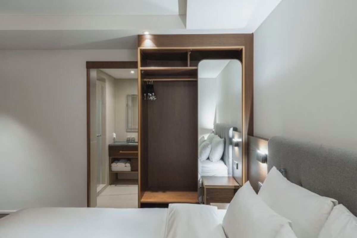 A modern hotel room with a bed, a nightstand, a mirror, and a wardrobe.