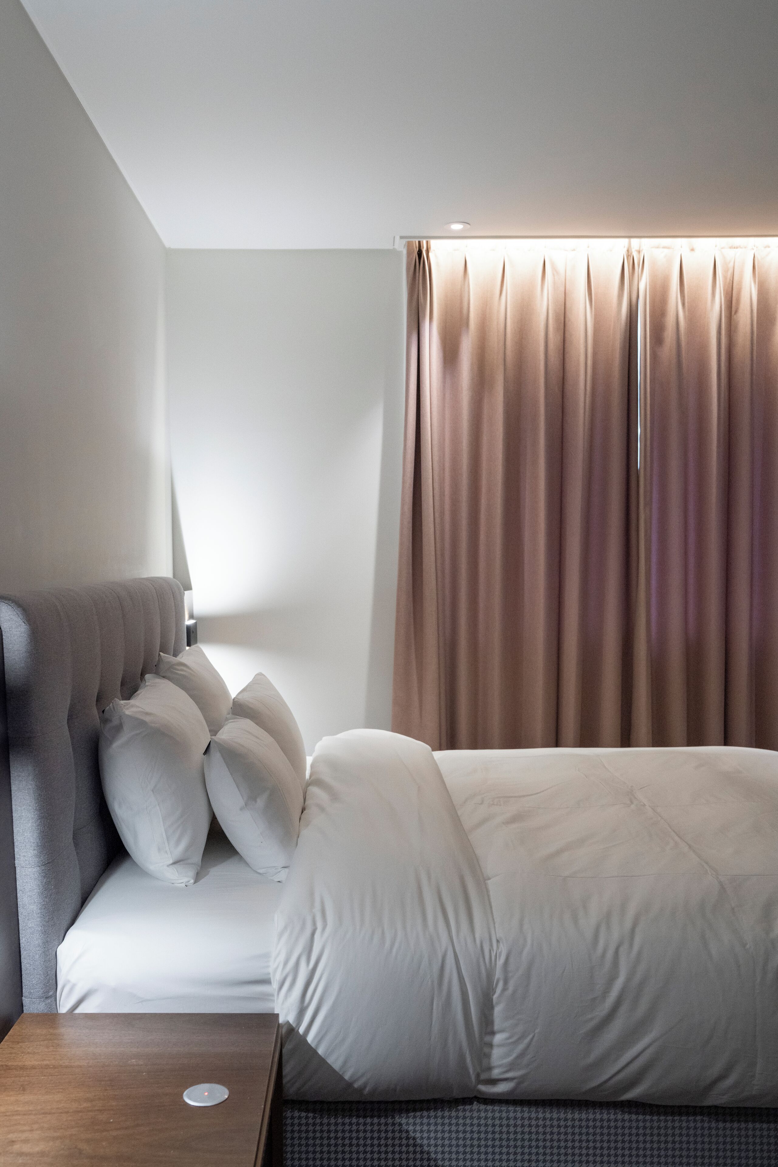 A neatly arranged hotel room with a bed, a bedside table, and a window with curtains.